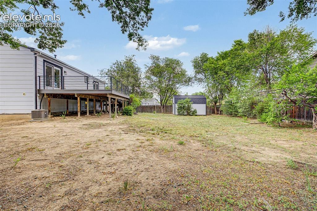 Image 34 of 44: Spacious backyard featuring a large wooden deck with black metal railings