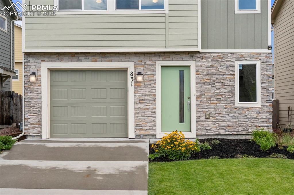 Image 2 of 22: Doorway to property with stone siding, a garage, and driveway