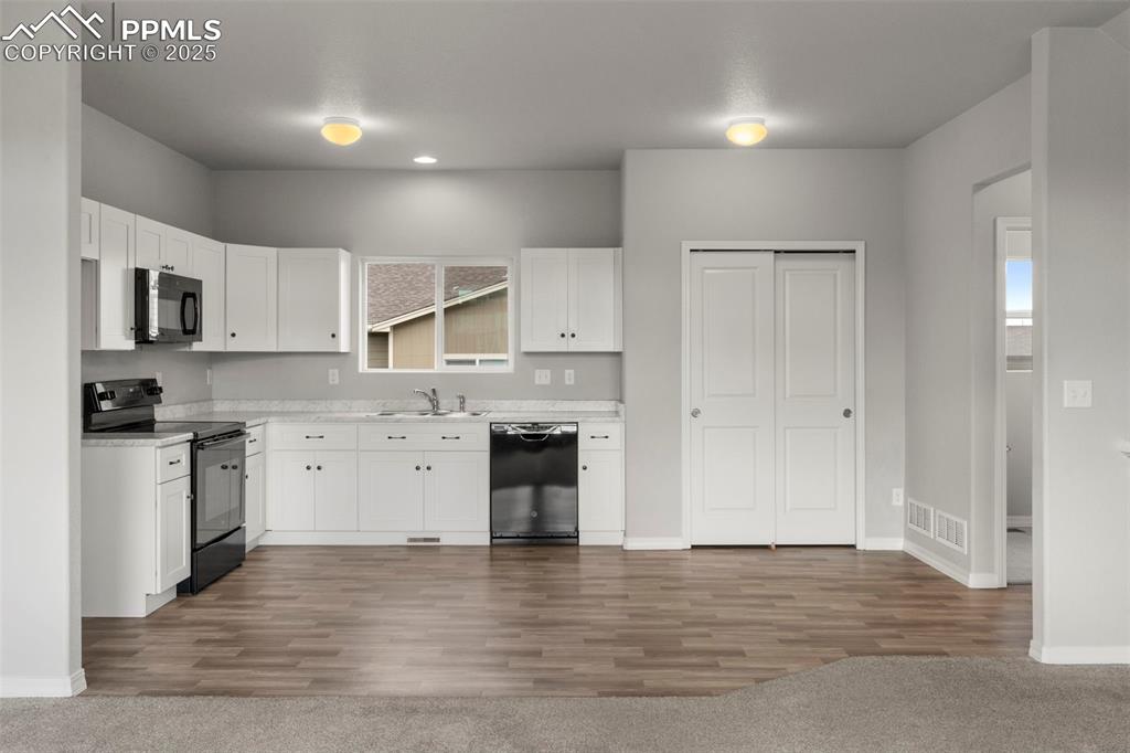 Image 9 of 22: Kitchen with black appliances, light countertops, white cabinets, and dark 