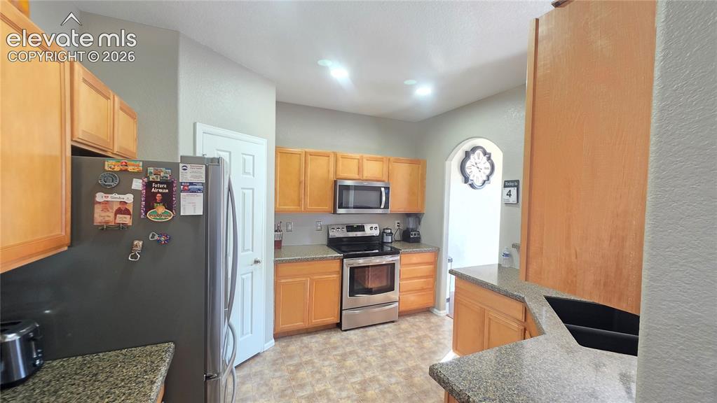 Image 8 of 35: Kitchen featuring wood cabinetry, stainless steel appliances, speckled coun