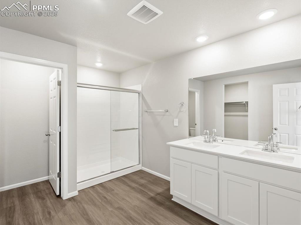 Image 18 of 25: Bathroom featuring double vanity, a stall shower, dark wood-style floors, a