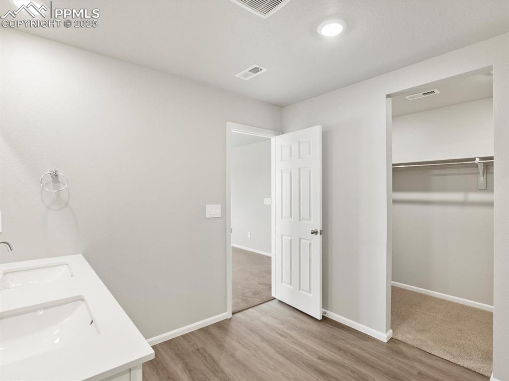 Image 19 of 25: Full bathroom with a walk in closet, double vanity, and light wood-type flo