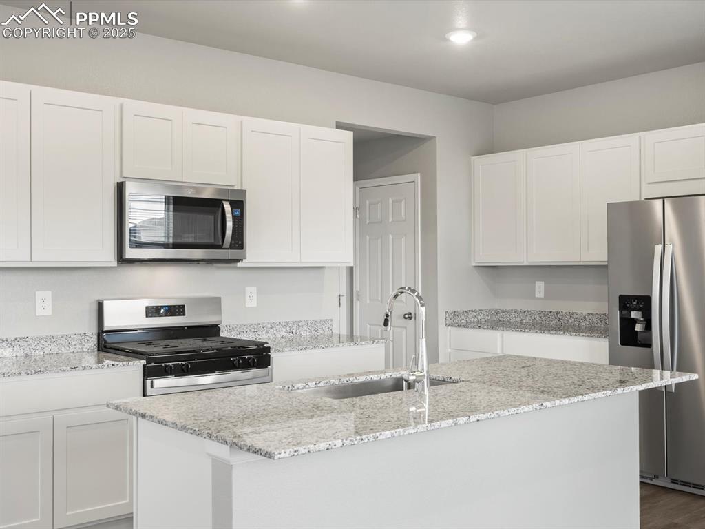 Image 4 of 25: Kitchen featuring stainless steel appliances, white cabinets, light stone c