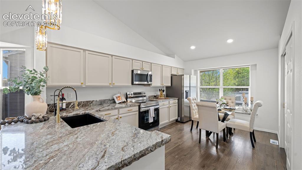 Image 14 of 46: Kitchen and dining area featuring vaulted ceilings, wood-finish flooring, s