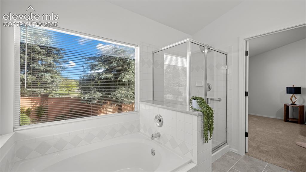 Image 24 of 46: Soaking tub with white tile surround, expansive window, glass-enclosed show