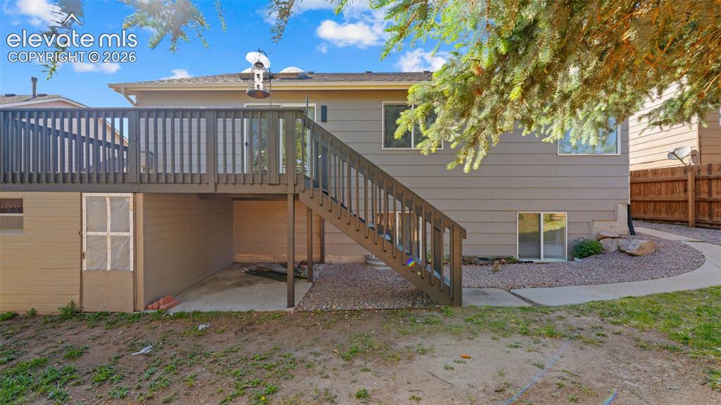 Image 34 of 46: Rear exterior featuring a spacious elevated deck with stairs, a concrete pa