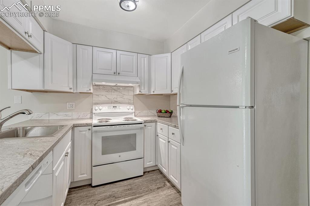 Image 10 of 50: Kitchen with white appliances, under cabinet range hood, a sink, and white