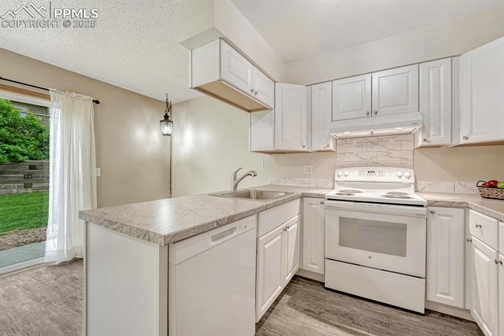 Image 11 of 50: Kitchen with white appliances, a sink, under cabinet range hood, light wood