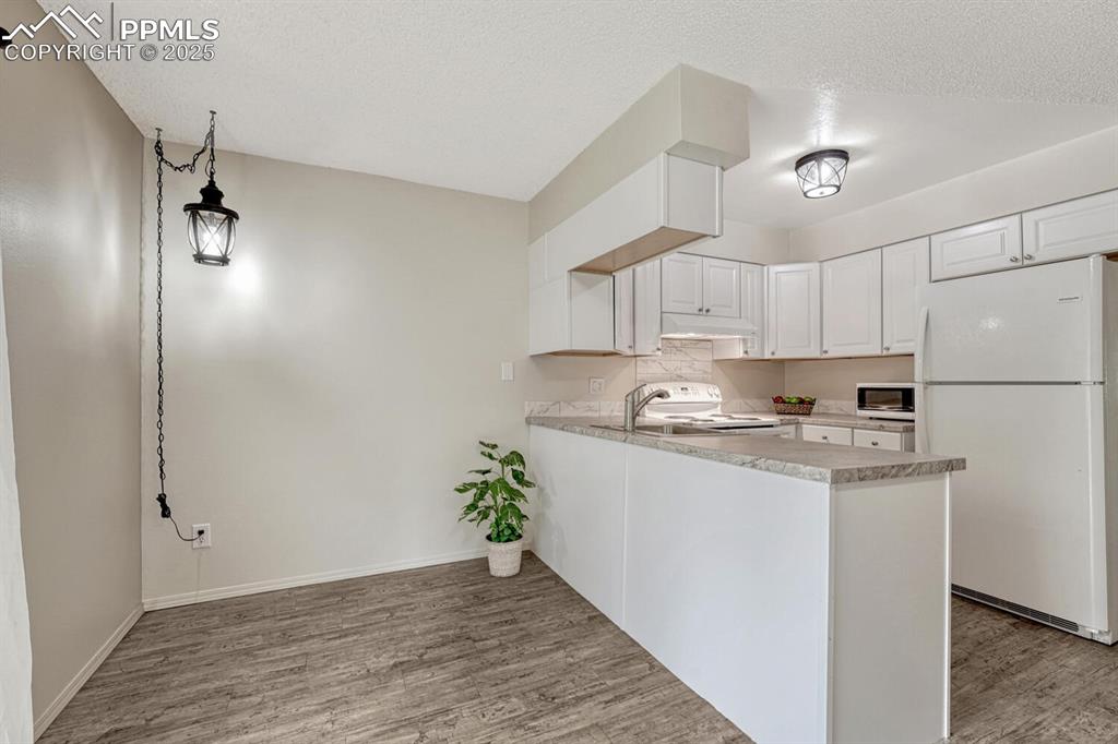 Image 12 of 50: Kitchen featuring white appliances, wood finished floors, under cabinet ran