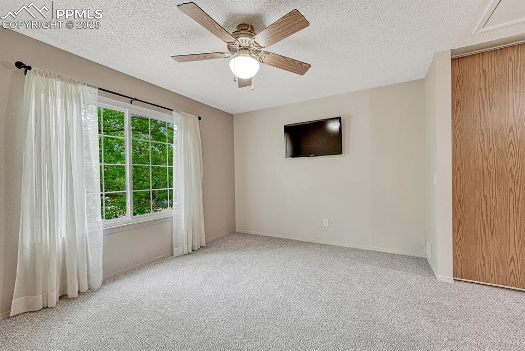 Image 26 of 50: Bedroom includes ceiling fan, curtains, and mounted TV
