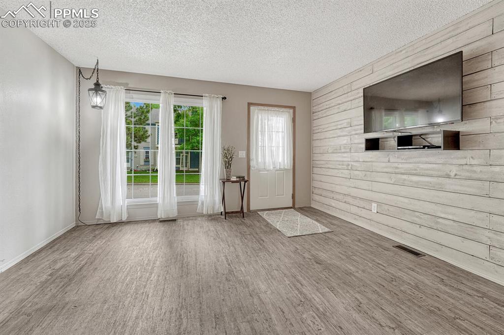 Image 3 of 50: Foyer entrance with wood finished floors, wooden walls, a textured ceiling,