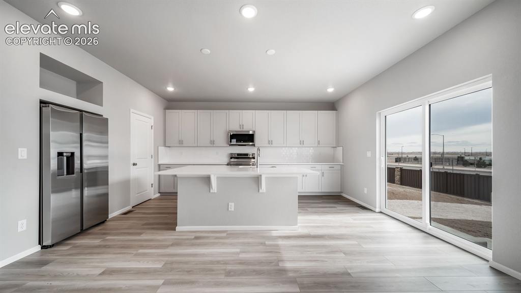 Image 12 of 34: Open-concept kitchen featuring an island, light wood-finish flooring, white
