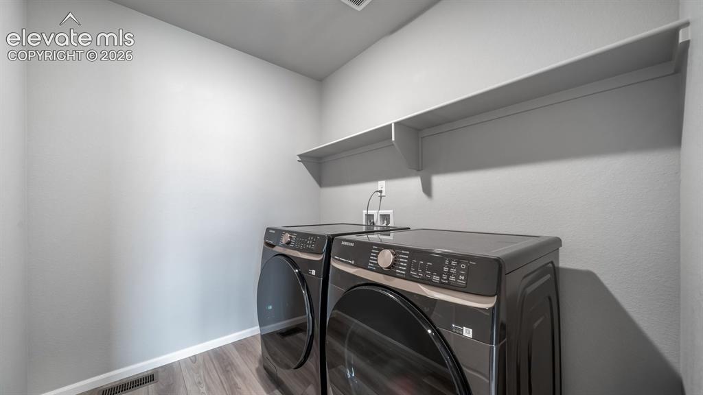 Image 32 of 34: Dedicated laundry area featuring a built-in wall shelf and wood-finish floo