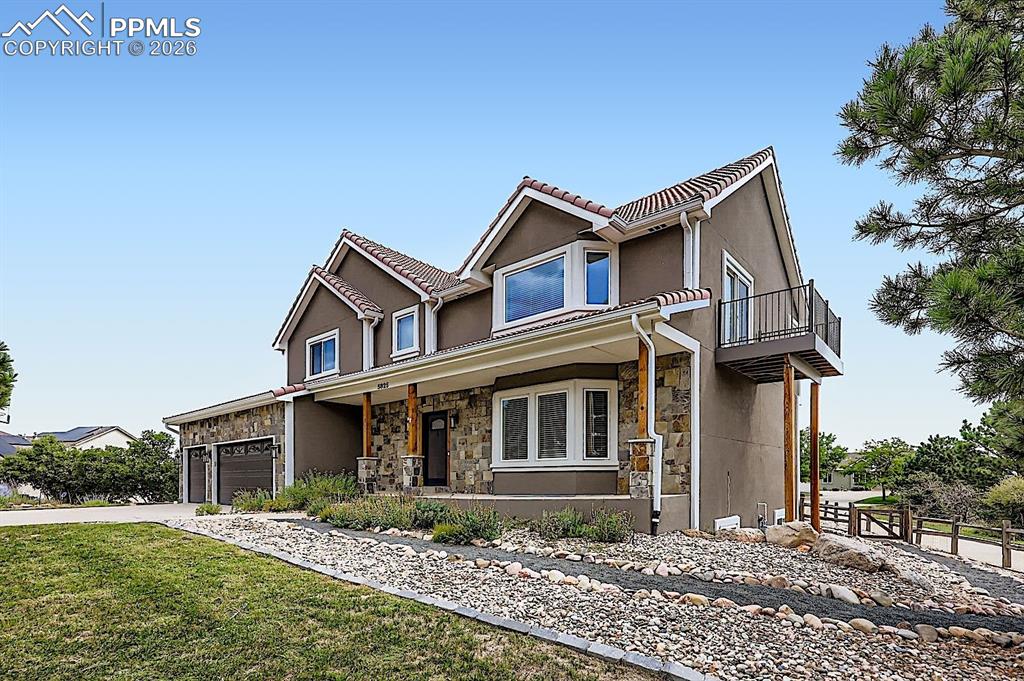 Caption: View of front facade with a garage, stone siding, stucco siding, and driveway