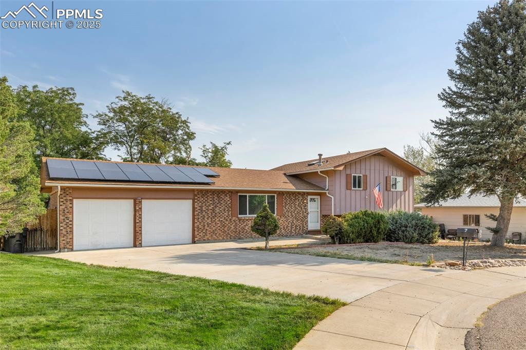 Caption: Tri-level home with roof mounted solar panels, concrete driveway, an attached garage, board and batt