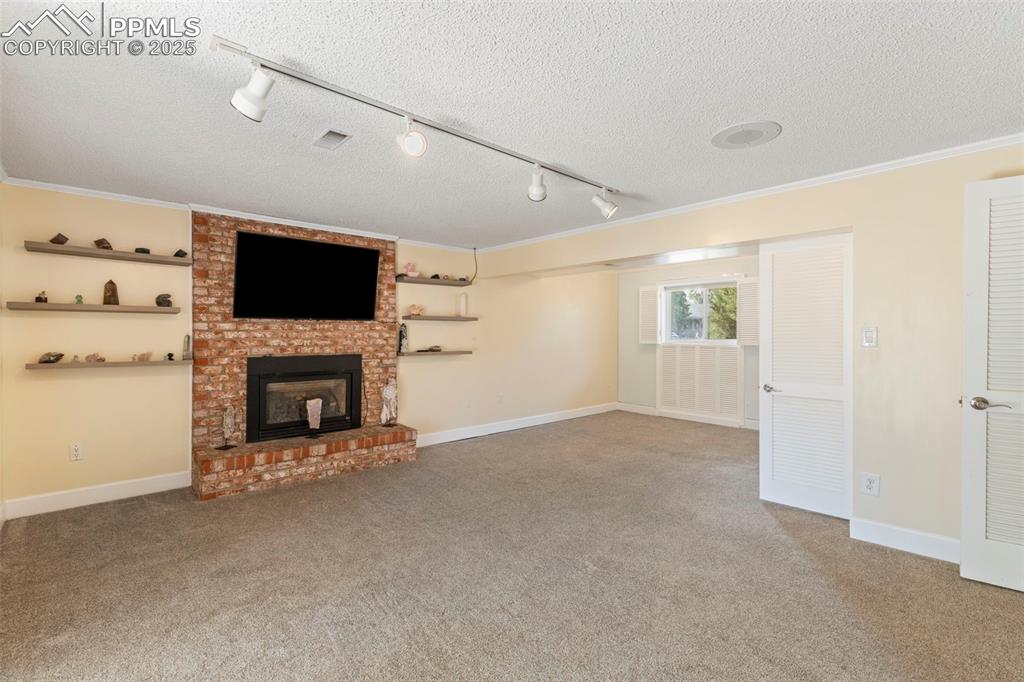 Image 16 of 32: Unfurnished living room featuring rail lighting, a textured ceiling, a bric