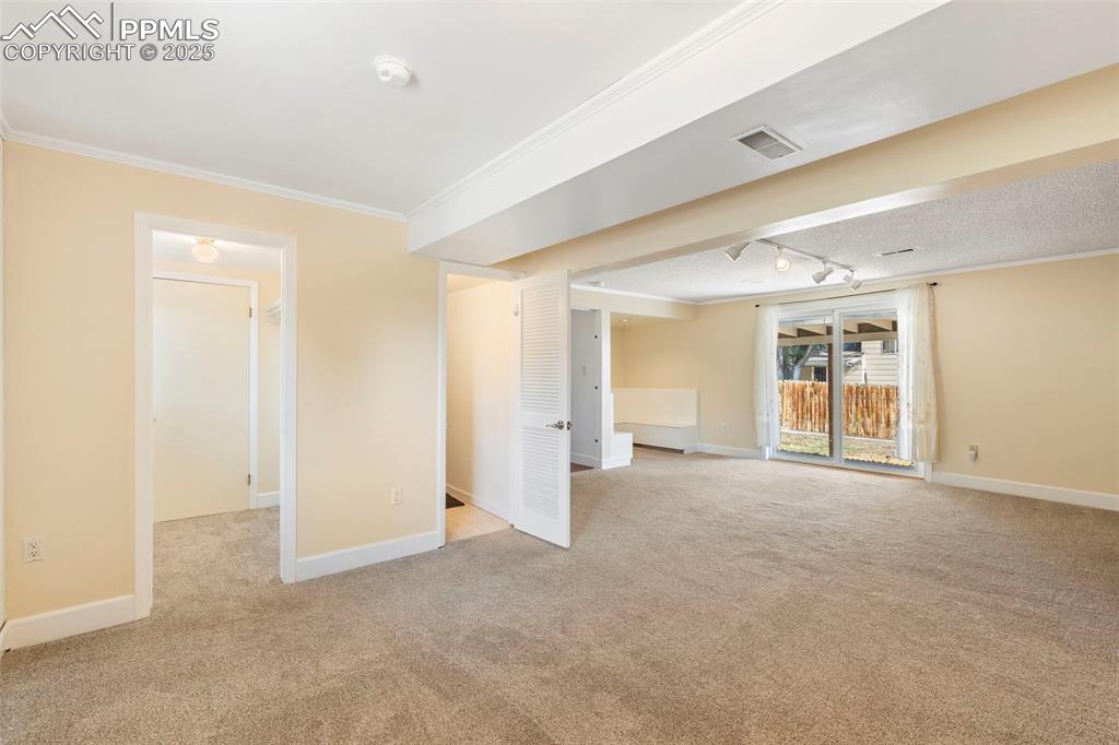 Image 17 of 32: Empty room with light colored carpet, crown molding, and track lighting