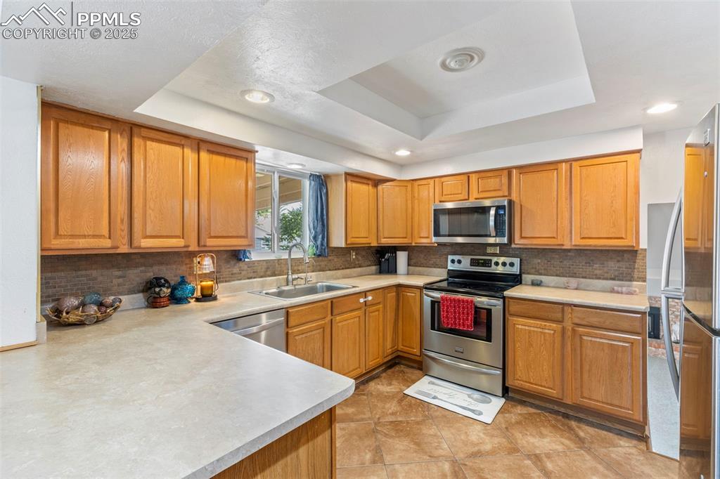 Image 8 of 32: Kitchen with backsplash, appliances with stainless steel finishes, a raised