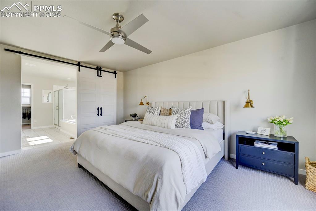 Image 18 of 50: Bedroom featuring a barn door, carpet, connected bathroom, and ceiling fan