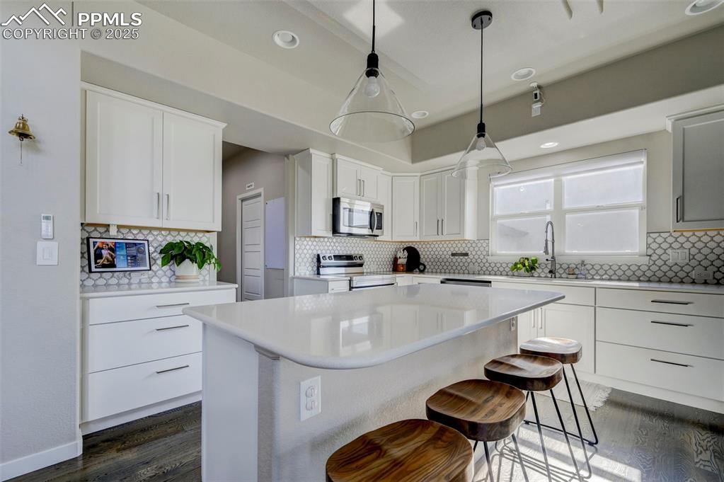 Image 36 of 50: Kitchen featuring backsplash, a breakfast bar area, pendant lighting, dark