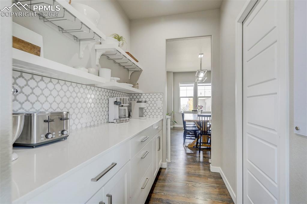 Image 38 of 50: Kitchen with open shelves, white cabinets, decorative backsplash, and dark