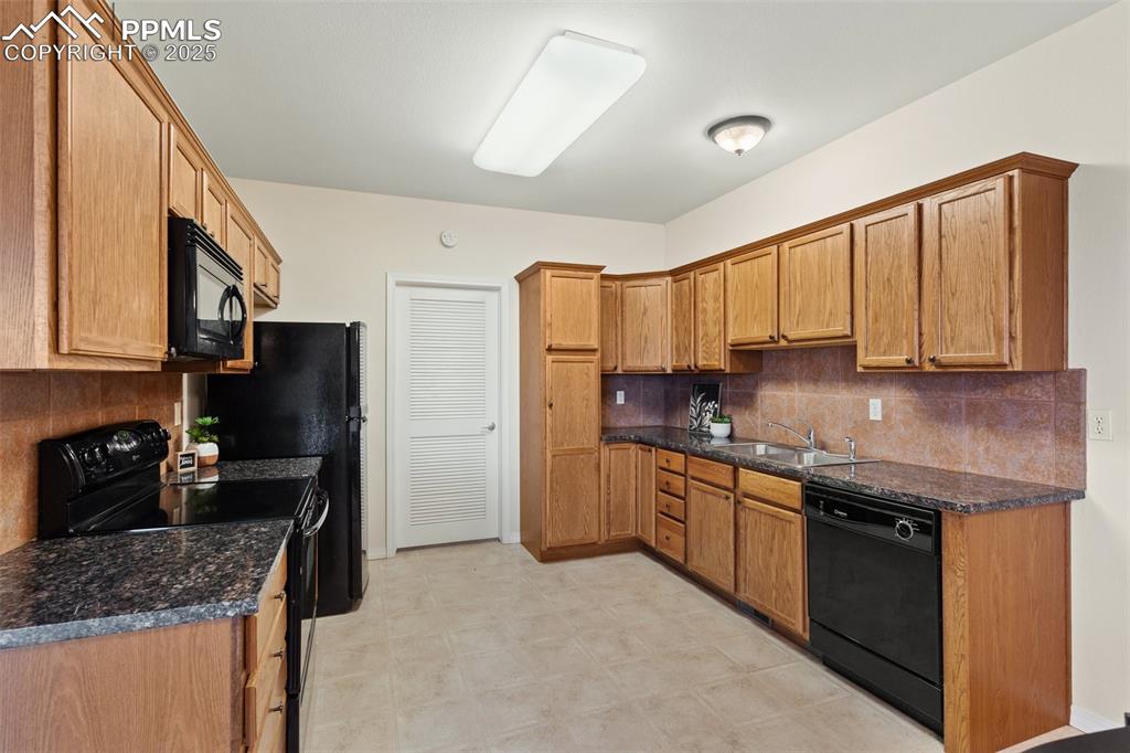 Image 10 of 27: Kitchen featuring tasteful backsplash, black appliances, dark stone counter