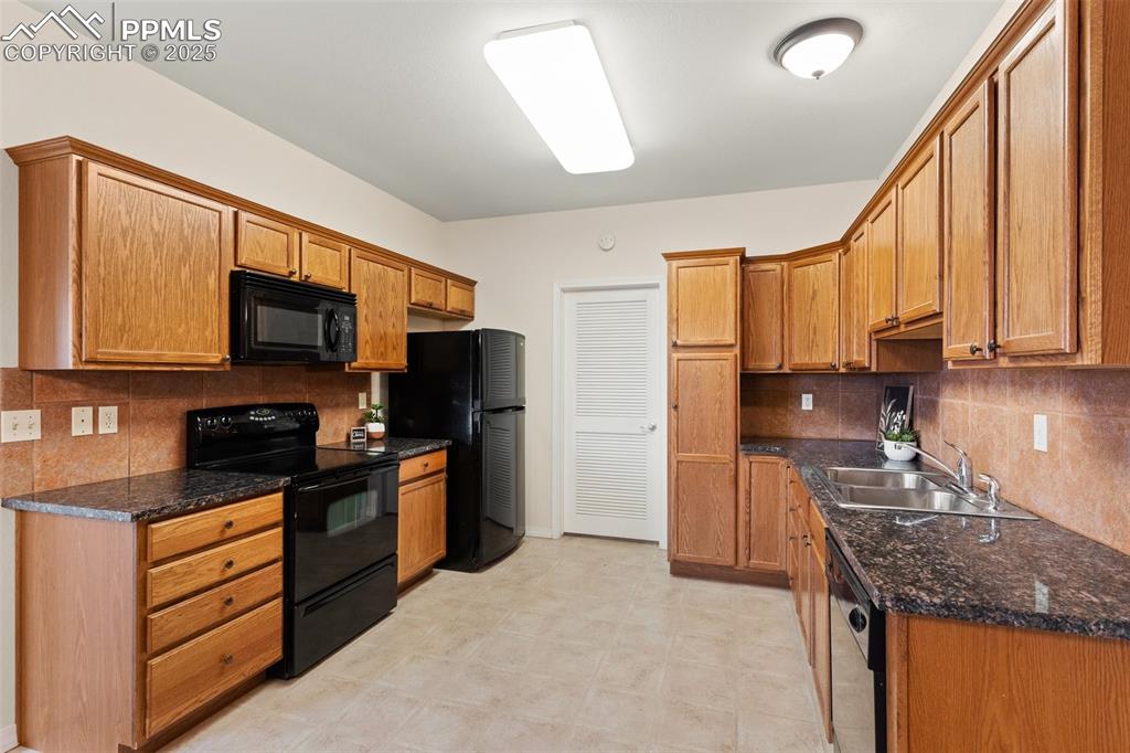 Image 12 of 27: Kitchen with backsplash, black appliances, dark stone countertops, and brow