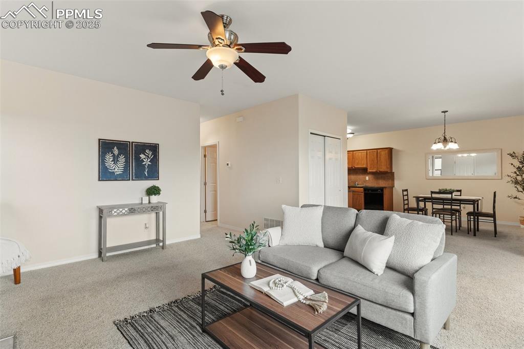Image 2 of 27: Living area with light carpet, a chandelier, and ceiling fan
