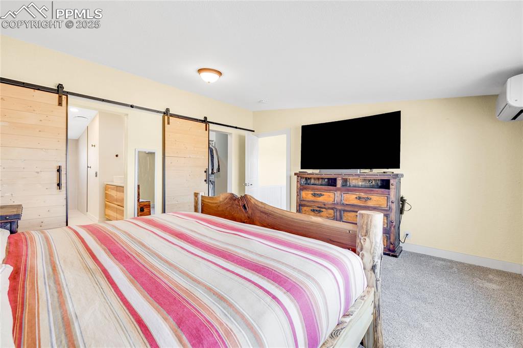 Image 18 of 49: Bedroom with a barn door, carpet floors, a wall mounted AC, and ensuite bat