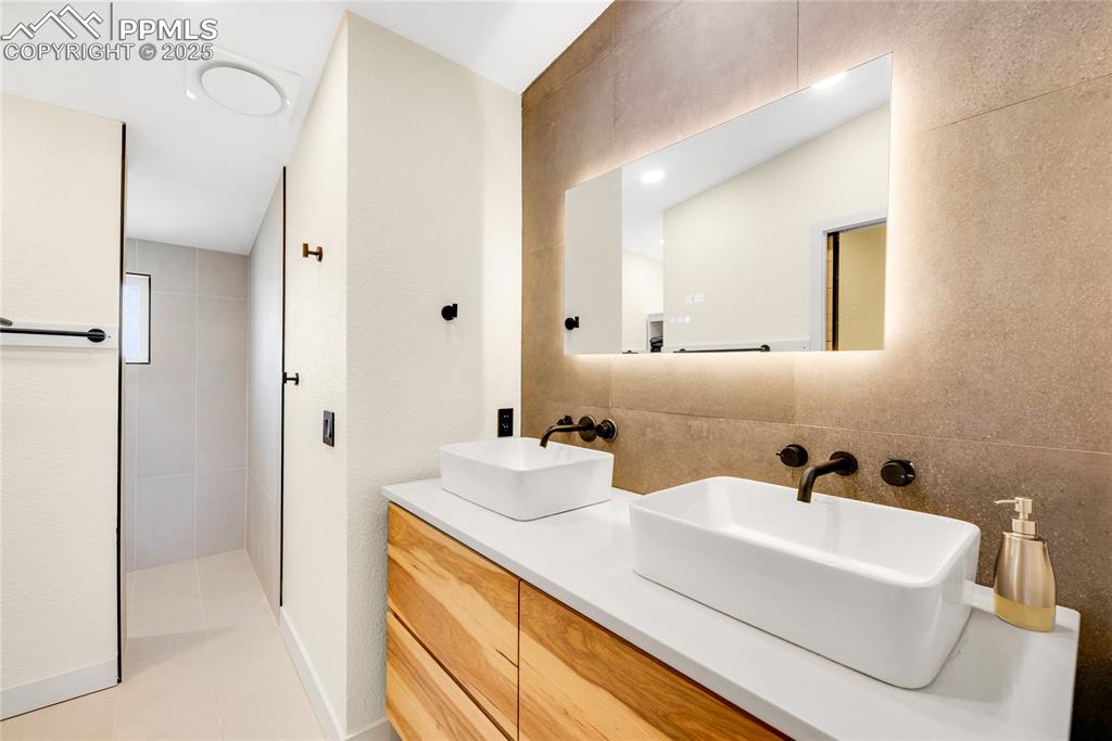 Image 20 of 49: Full bath with double vanity, tile walls, light tile patterned floors, and 
