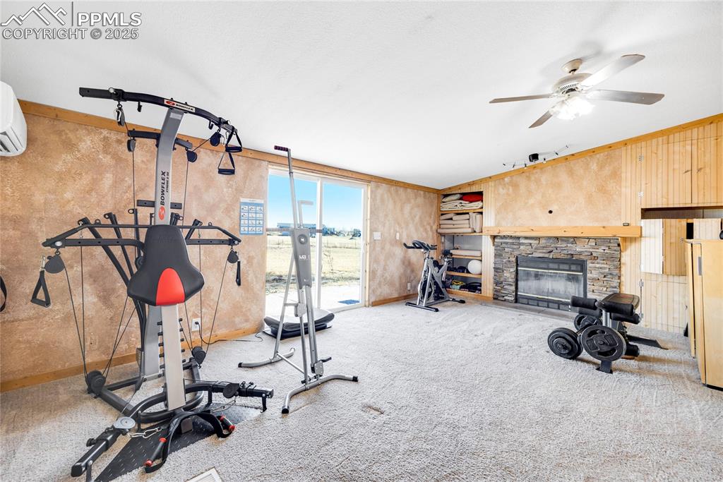 Image 23 of 49: Exercise area with a fireplace, carpet, an AC wall unit, a ceiling fan, and