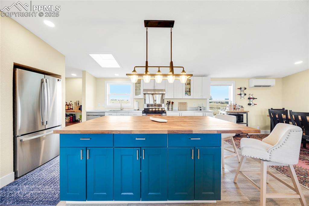 Image 5 of 49: Kitchen featuring blue cabinetry, a skylight, glass insert cabinets, a cent