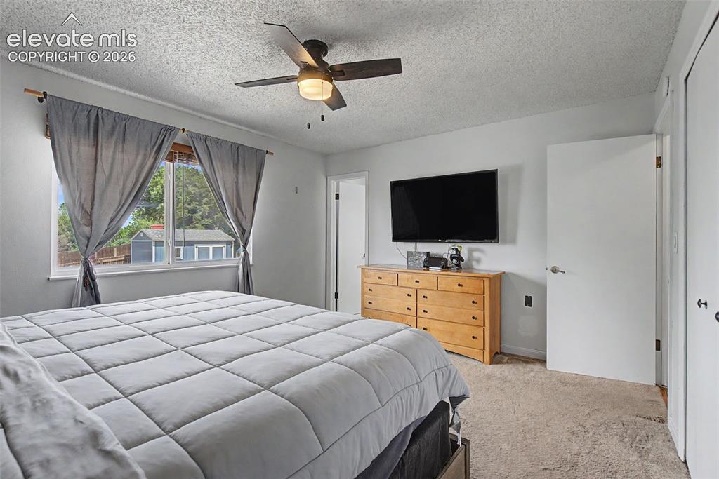 Image 16 of 30: Carpeted bedroom with a window offering exterior views, a ceiling fan with