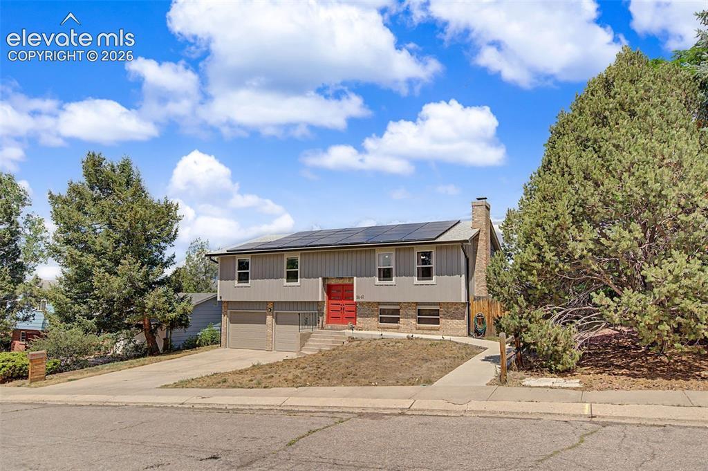 Image 2 of 30: Split-level residence featuring a gray facade with a bold red front door, p
