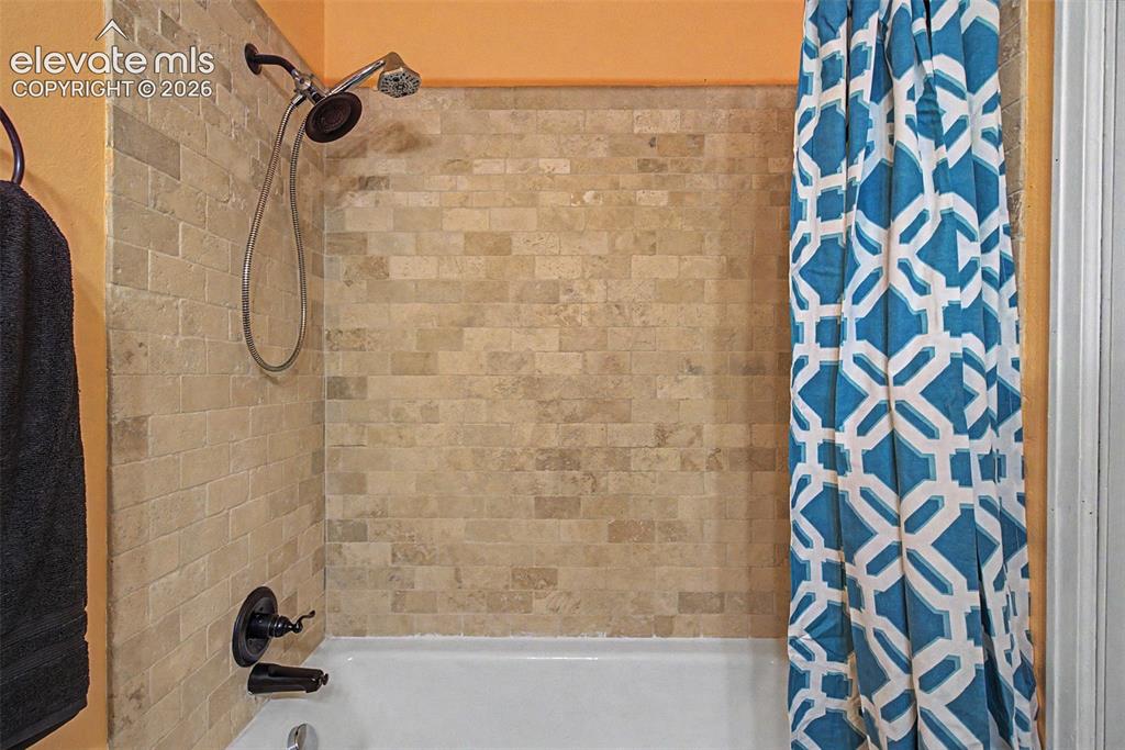 Image 21 of 30: Bathtub and shower combination featuring subway tile surround, a dark bronz