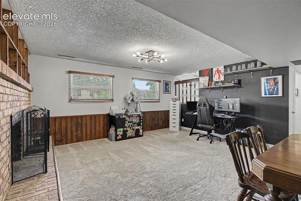 Image 23 of 30: Spacious living area featuring a brick fireplace, wood paneling, light grey