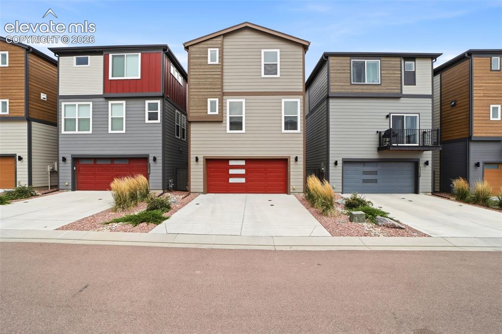 Caption: Contemporary three-story exterior featuring multi-toned siding, a red garage door, and a concrete dr