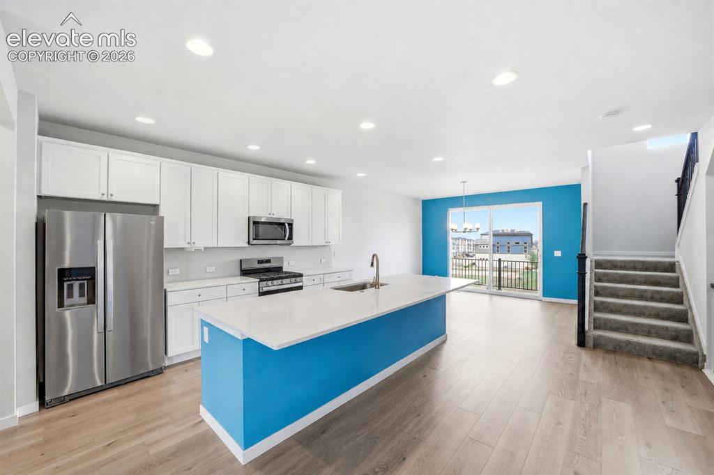 Image 12 of 23: Modern kitchen featuring white cabinetry, stainless steel appliances, a lar