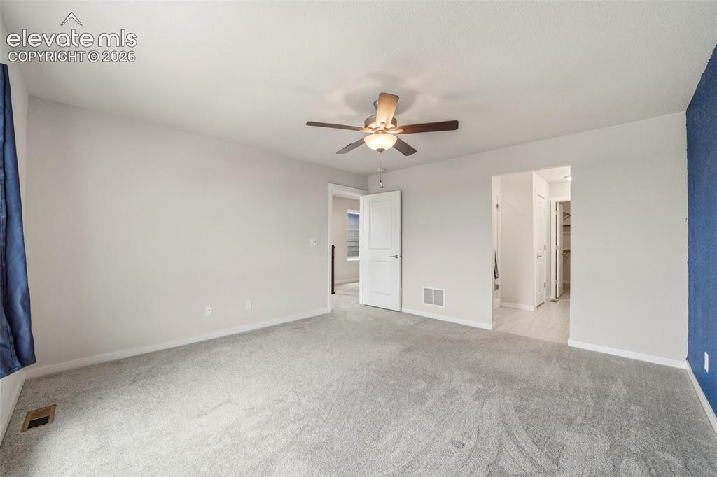 Image 18 of 23: Spacious room with light gray carpeting, a ceiling fan with light fixture, 