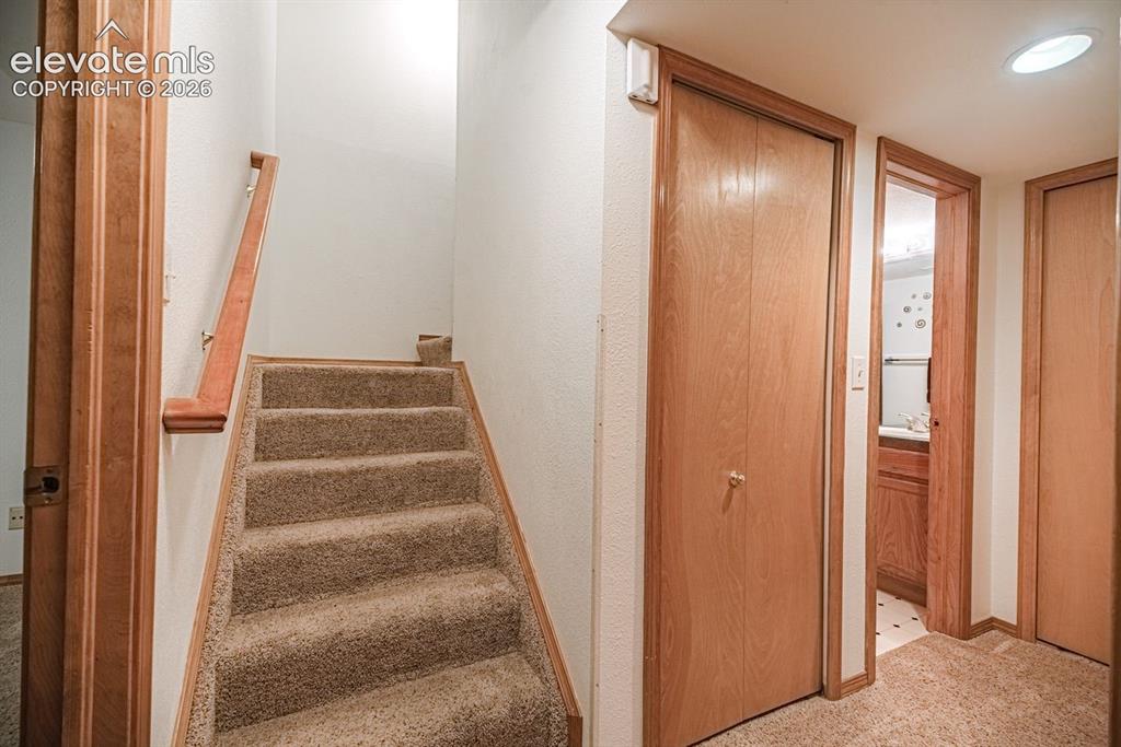 Image 32 of 38: Carpeted staircase with wood-finish handrail, surrounded by white walls and