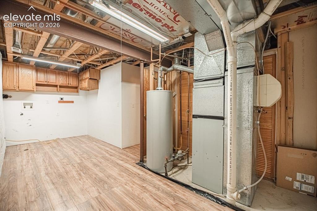 Image 34 of 38: Utility room with wood-finish flooring, white walls, and wood cabinetry