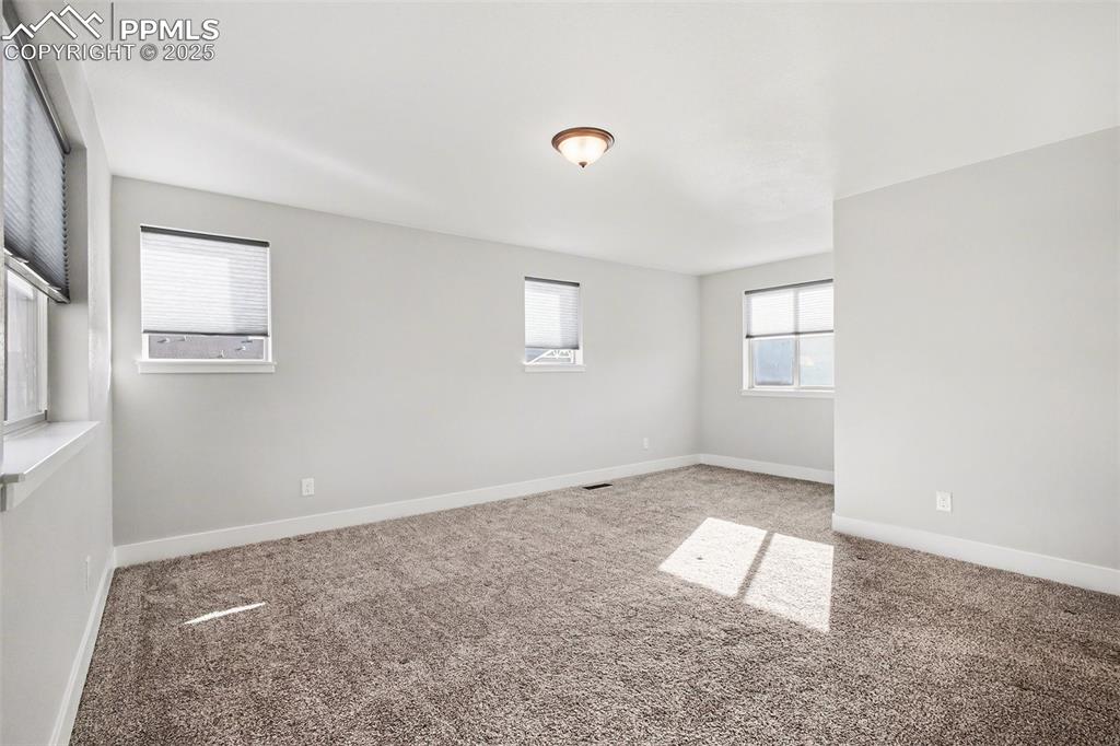Image 13 of 20: Large carpeted primary bedroom with lots of windows making it bright and in