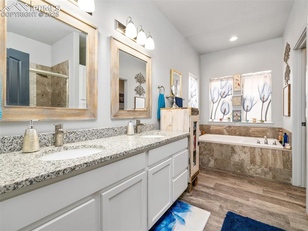 Image 16 of 25: Full bath featuring a garden tub, a shower stall, double vanity, and wood f