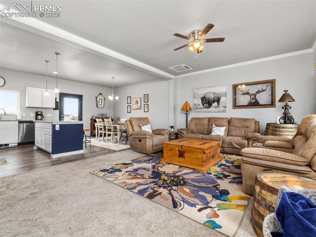 Image 2 of 25: Carpeted living room with ceiling fan, crown molding, and a chandelier