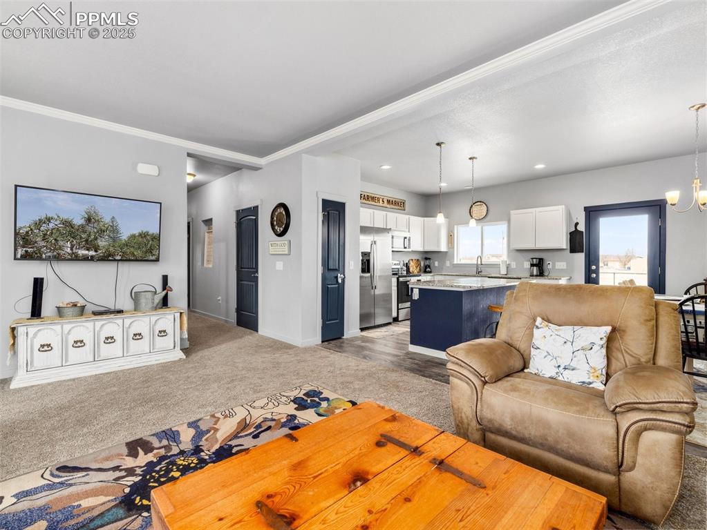 Image 5 of 25: Living area with a chandelier, light carpet, crown molding, and recessed li