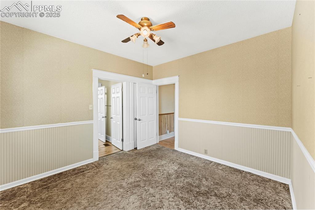 Image 12 of 27: Spare room featuring carpet flooring, ceiling fan, wainscoting, and wallpap