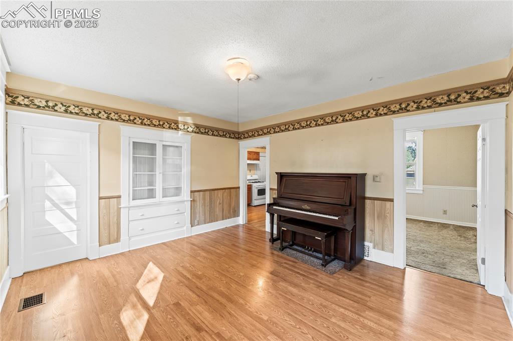 Image 13 of 27: Sitting room featuring a textured ceiling, wainscoting, light wood finished