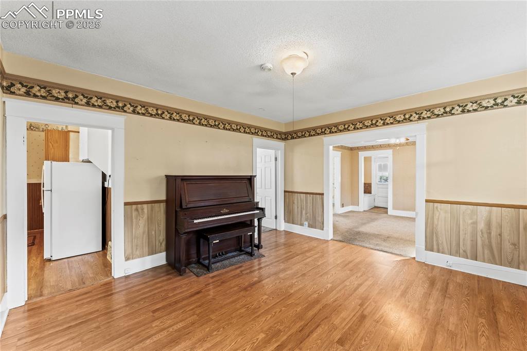 Image 14 of 27: Living area with wainscoting, a textured ceiling, and wood finished floors