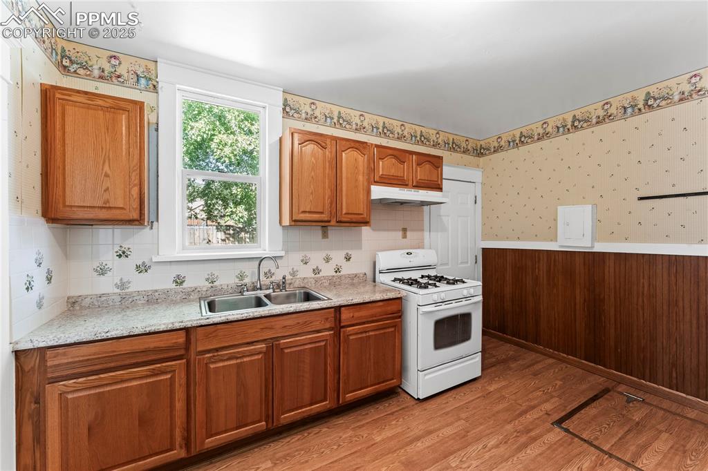 Image 16 of 27: Kitchen with wallpapered walls, white gas stove, light wood finished floors