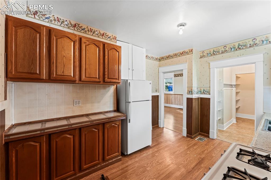 Image 17 of 27: Kitchen featuring light wood-style flooring, brown cabinets, a wainscoted w